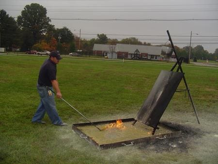 A man igniting a flame in an outdoor fire pit using a torch.