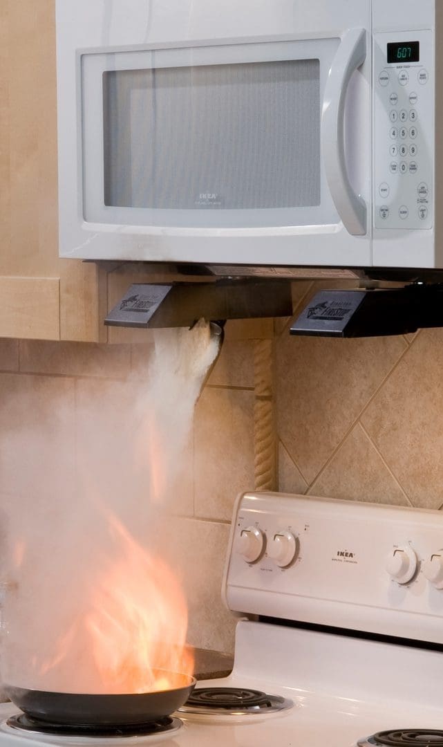 Fire igniting on a stove beneath a microwave in a kitchen.