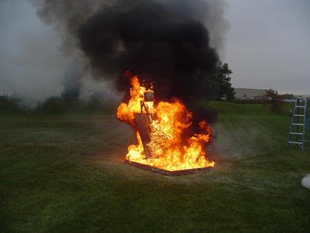 A large fire burns intensely outdoors with thick black smoke.