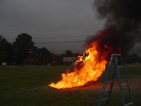 A large fire burns intensely outdoors with thick black smoke rising.