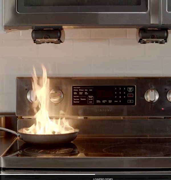 Flames flare up from a frying pan on a stove during cooking.