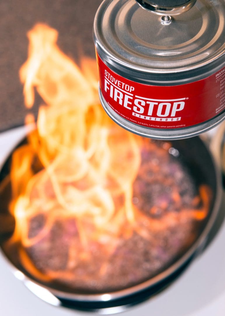 A can of Fire Stop foam held near a flaming pan on a stove.