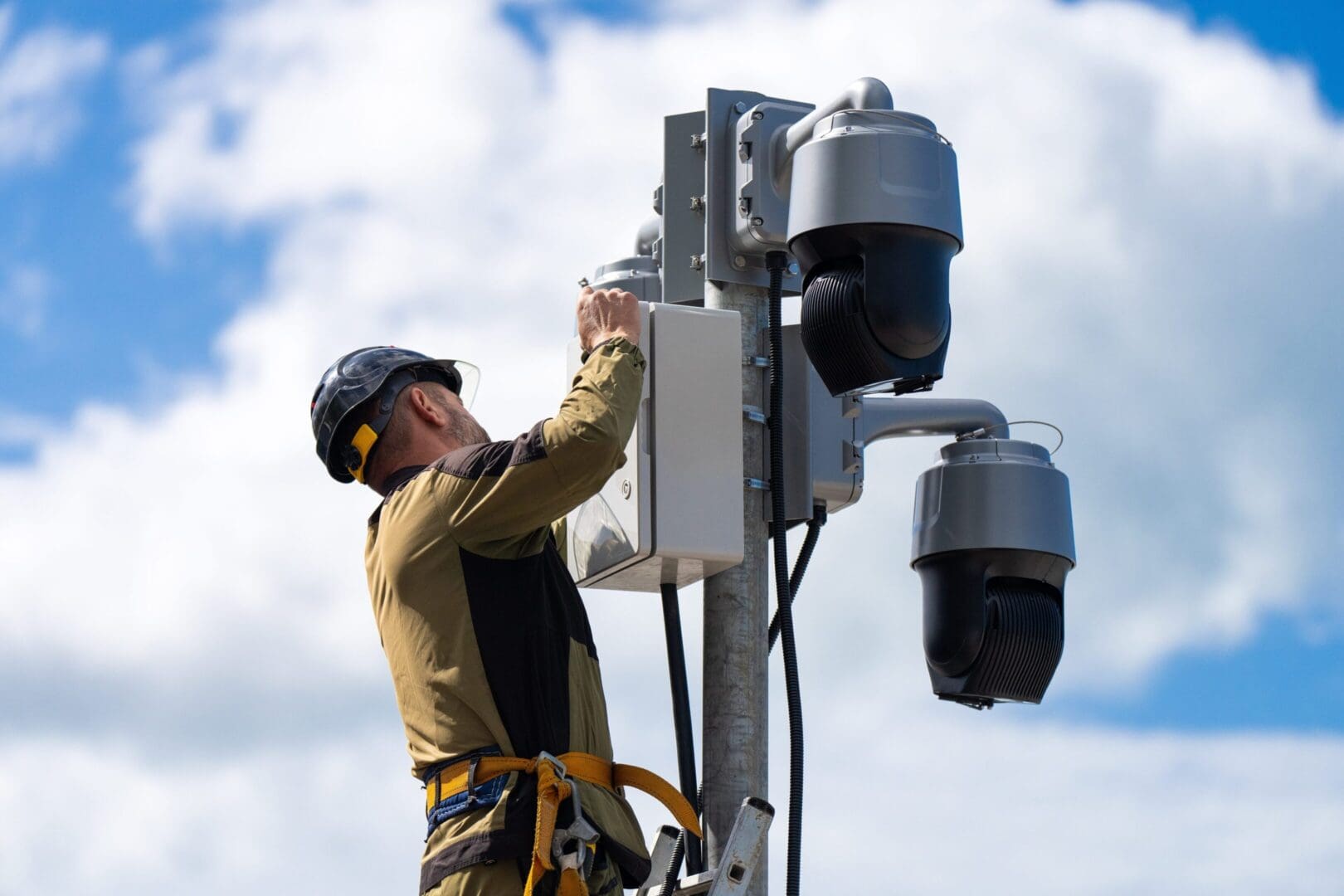 Technician installing or repairing security cameras on a pole outdoors.